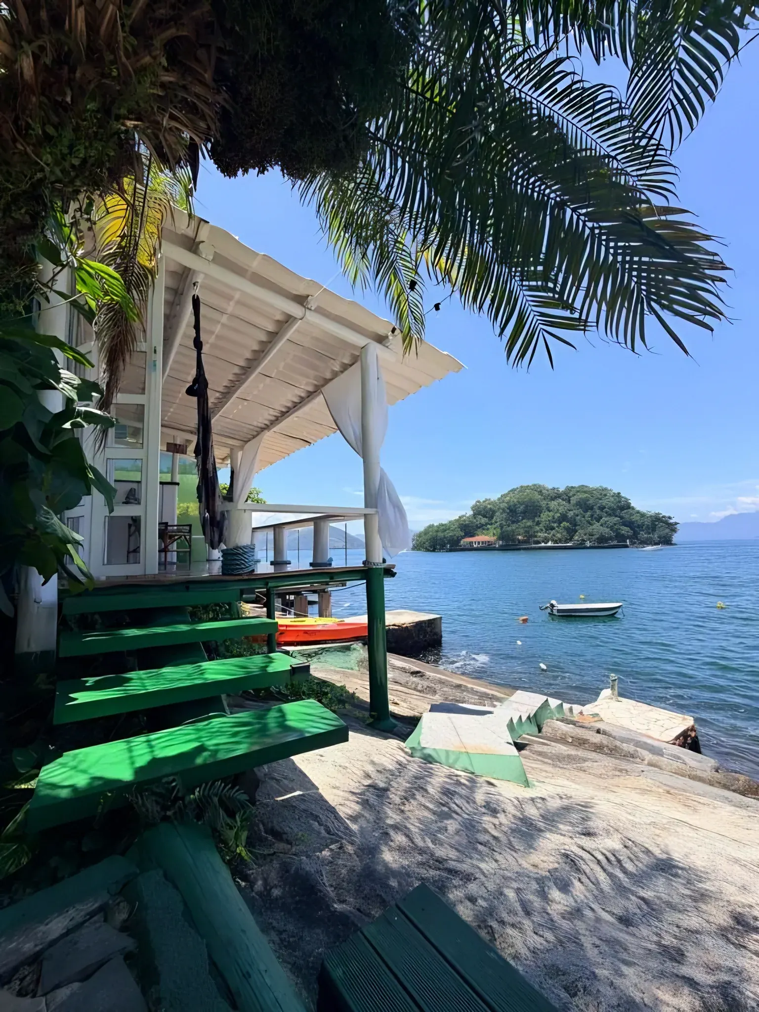 Escada verde descendo da varanda até o mar, com uma ilha em frente