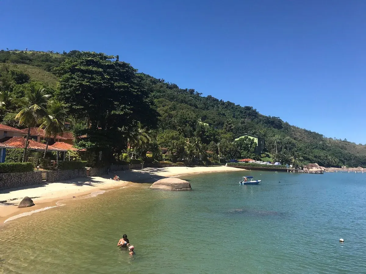Praia curta ao pé do morro, com um barco parado na água