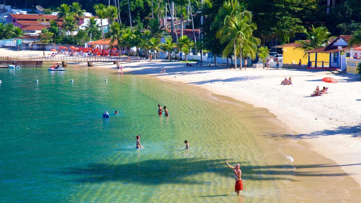 Praia de areia branca e água verde-clara, com coqueiros e casas na orla