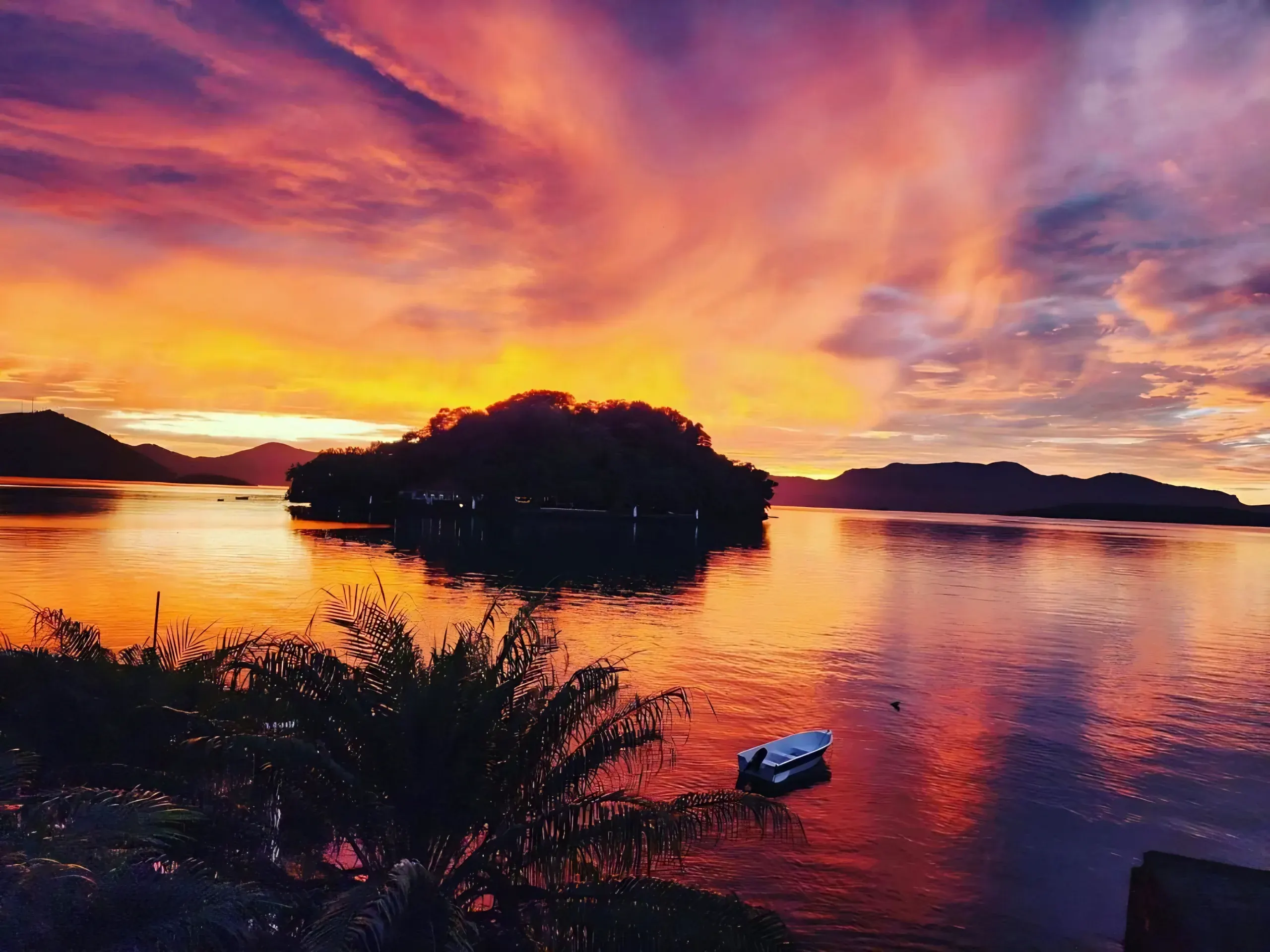 Pôr do sol alaranjado sobre a ilha em frente à pousada, com um barco na água