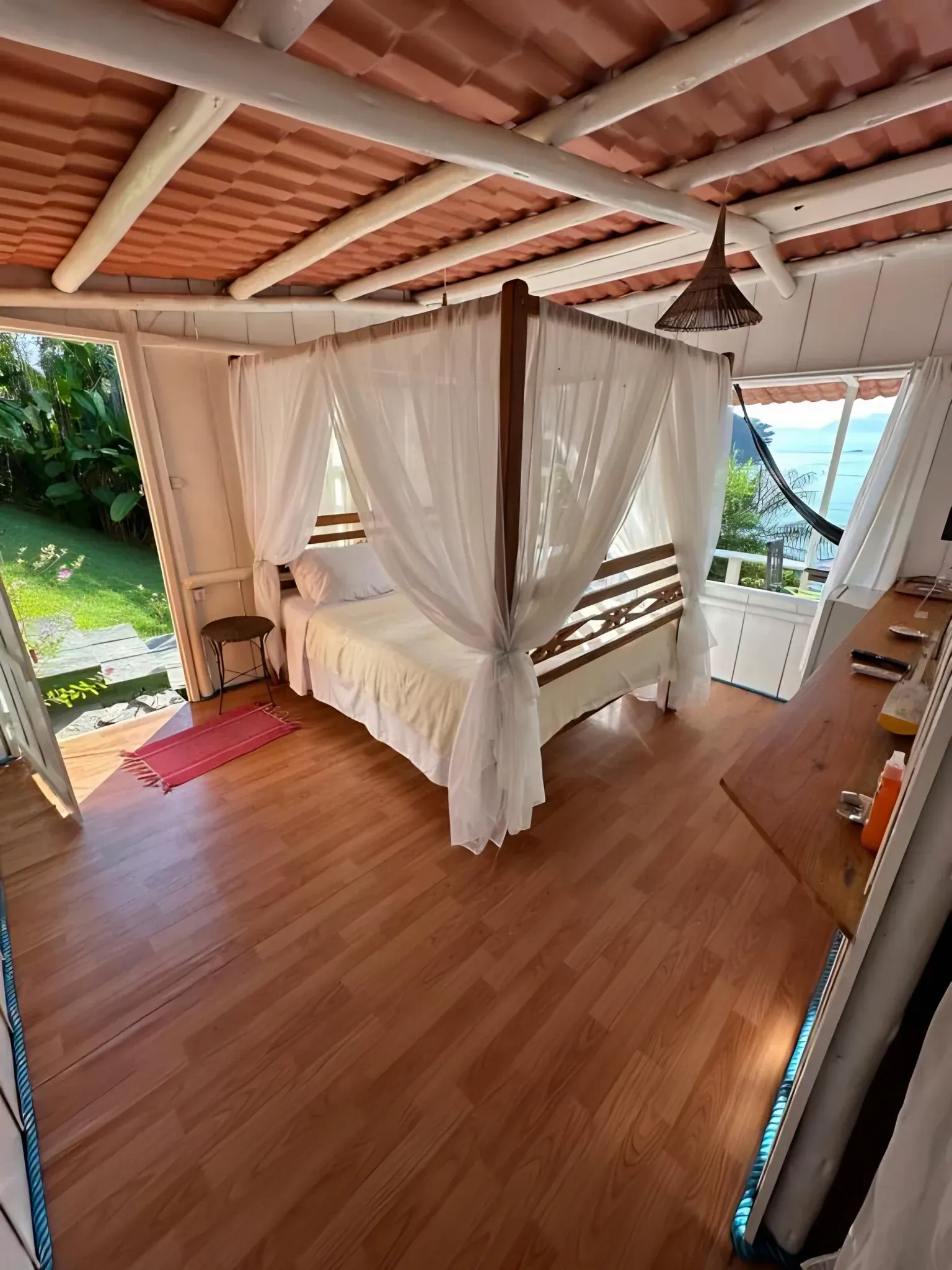 Quarto com cama de dossel, piso de madeira e janela para o mar